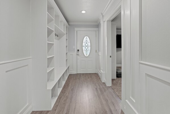 A hallway with white walls, a wooden floor, and a door with a decorative glass panel.