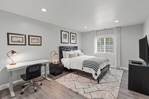 Une chambre à coucher comprenant un lit, un bureau, une chaise, des tables de chevet et un téléviseur.