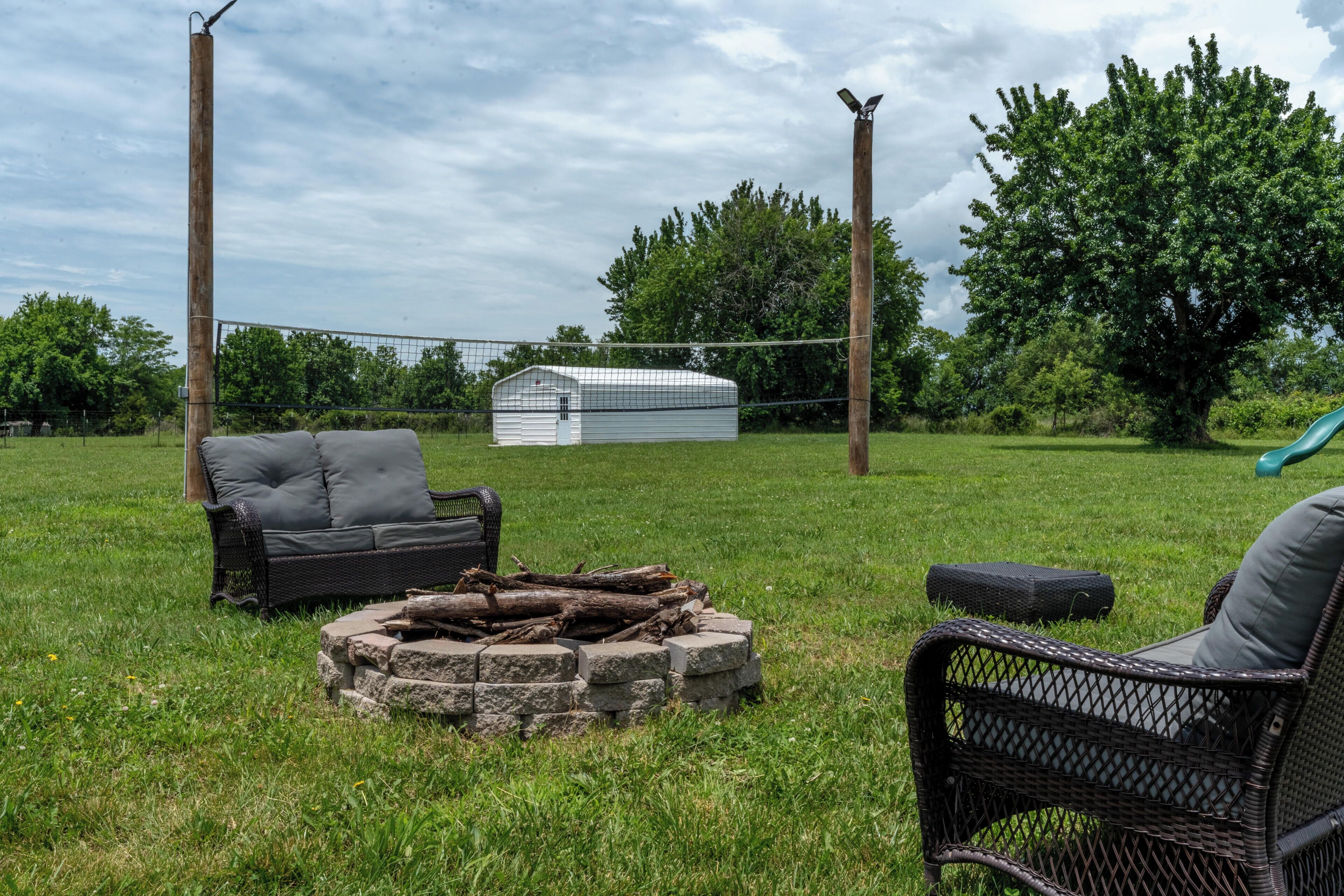 A grassy outdoor area with a white shed, a black wicker chair, and a fire pit.