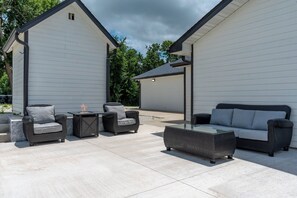 Ein möblierter Patio mit Korbmöbeln, darunter eine Couch und Stühle, sowie ein Couchtisch mit Glasplatte.