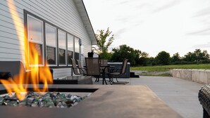 Eine Terrasse mit Feuerstelle, Gartenmöbeln und Blick auf ein Haus.