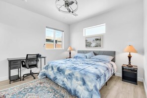 Un dormitorio con cama, escritorio, silla, dos lámparas de noche, ventilador de techo y ventana.