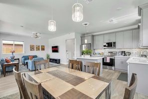 Una cocina moderna con armarios blancos, un microondas y un lavamanos. Hay una zona de comedor con una mesa y sillas de madera.