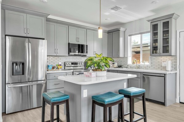 Una cocina moderna con armarios grises, electrodomésticos de acero inoxidable, una isla central con taburetes y una lámpara colgante.