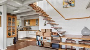 Una cocina moderna con armarios de madera, una estantería empotrada y una escalera con vigas a la vista.
