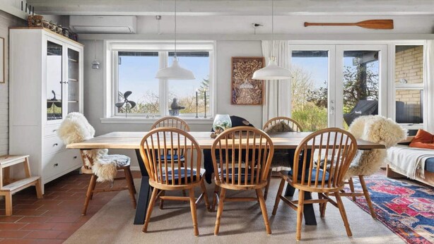 Un comedor con una mesa de madera, cuatro sillas, un tapete y vistas al exterior.