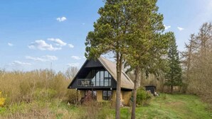 Una casa con techo inclinado, balcón y un área verde circundante con árboles.