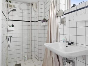 A bathroom with white tiled walls, a shower, a sink, and a mirror.