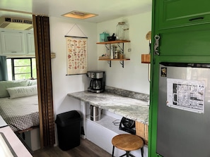 Cocina compacta con cafetera, un cubo de basura, un taburete pequeño y un refrigerador con un mapa.