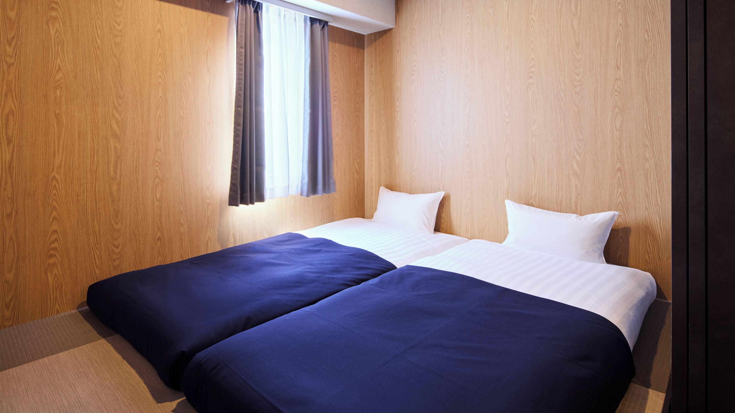A hotel room with a wooden wall, a window with curtains, and a bed with two pillows.
