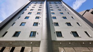 A tall building with a central cylindrical structure, multiple windows, and a tiled facade. - Minn Hakata Station East (Fukuoka)