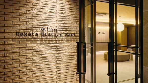 A brick wall with the text 'Hakata Station East' and 'Minn' indicating the hotel's name.