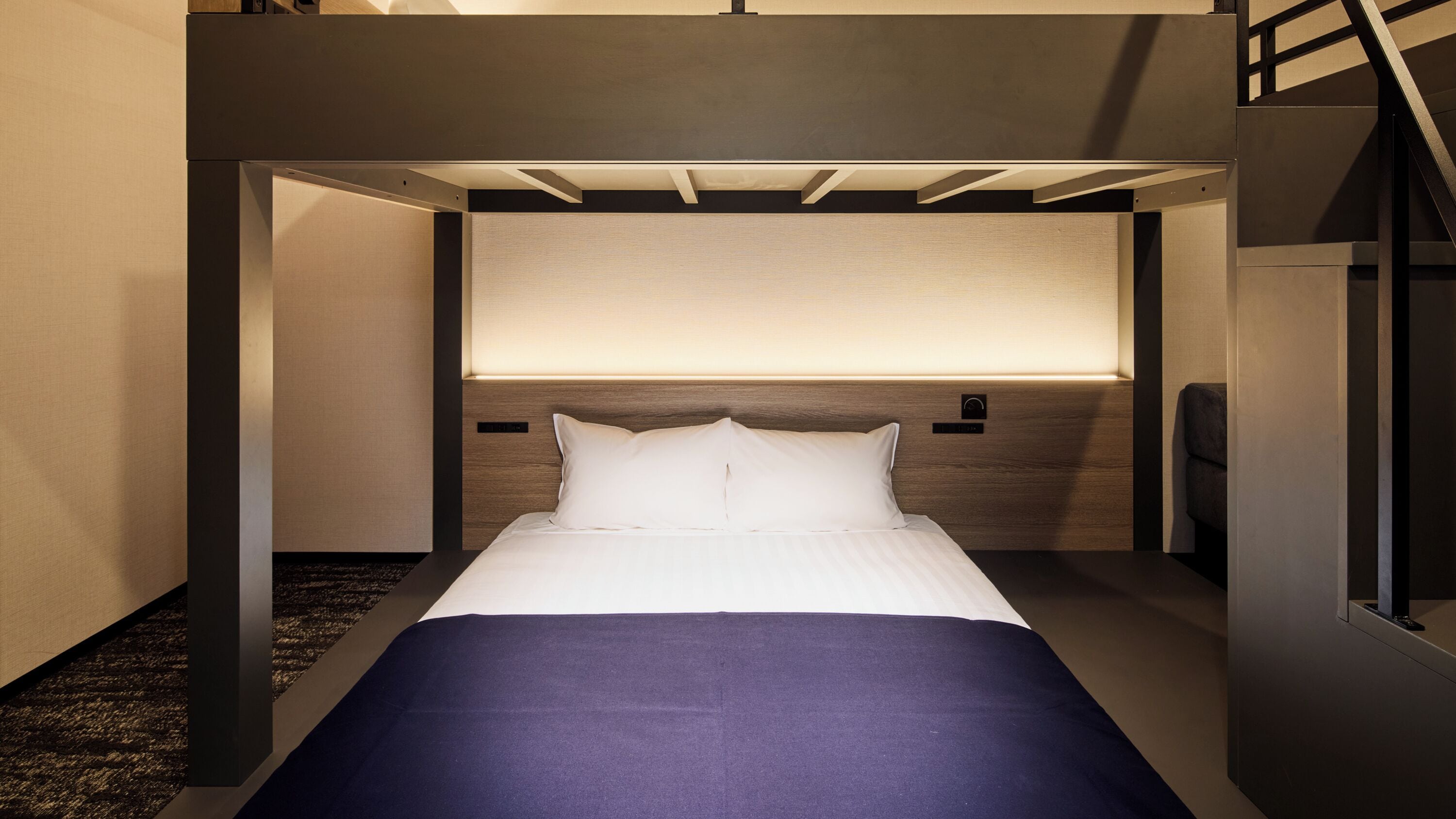 Habitación de hotel moderna con cama, cabecera con panel de luz y alfombra oscura.