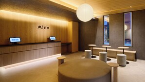 A hotel reception area with a wooden reception desk, a seating area with round tables, and a large round seating piece in the center. - Minn Hakata Station East (Fukuoka)