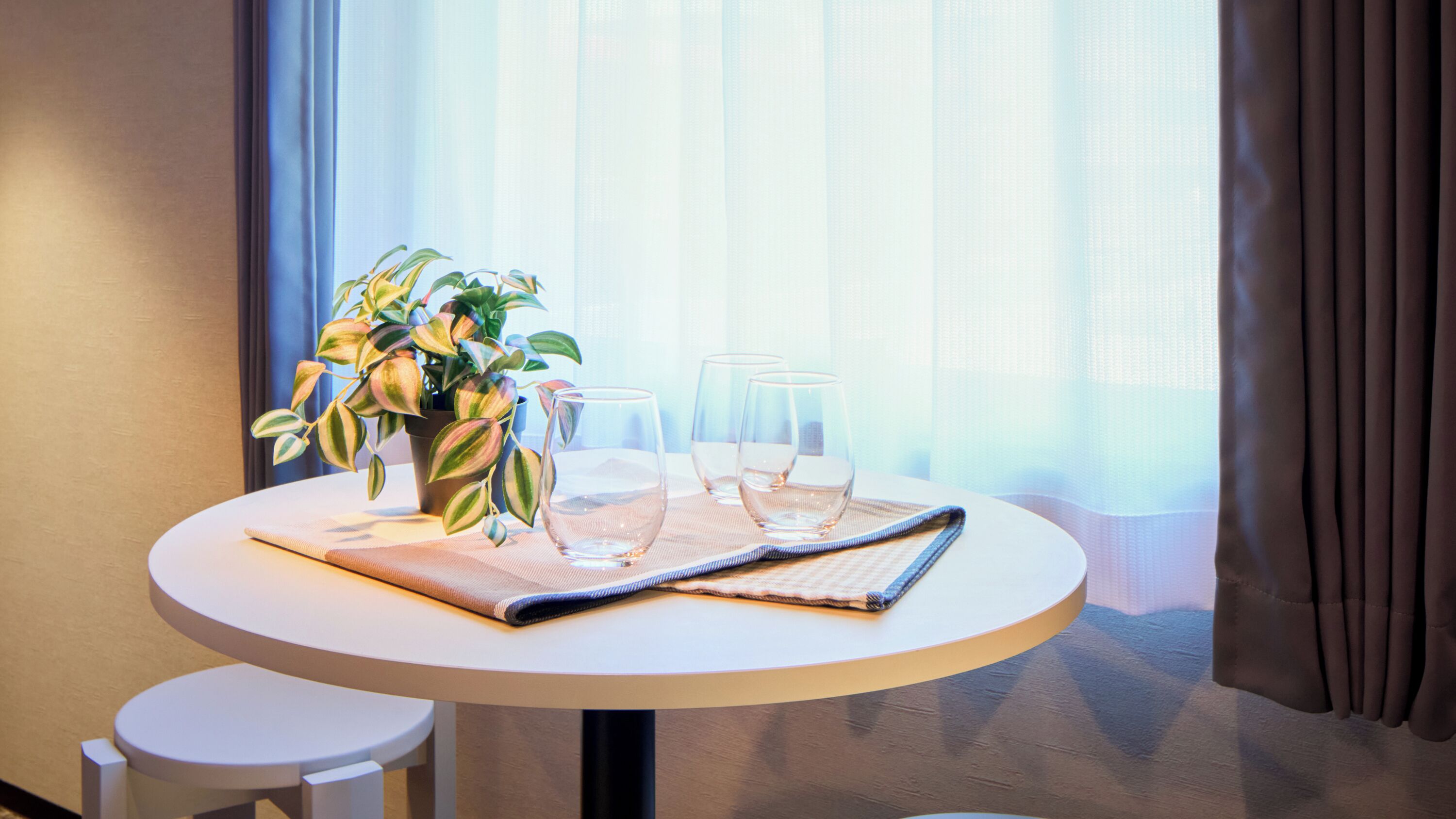 A round table with a potted plant, three glasses, and a folded napkin.