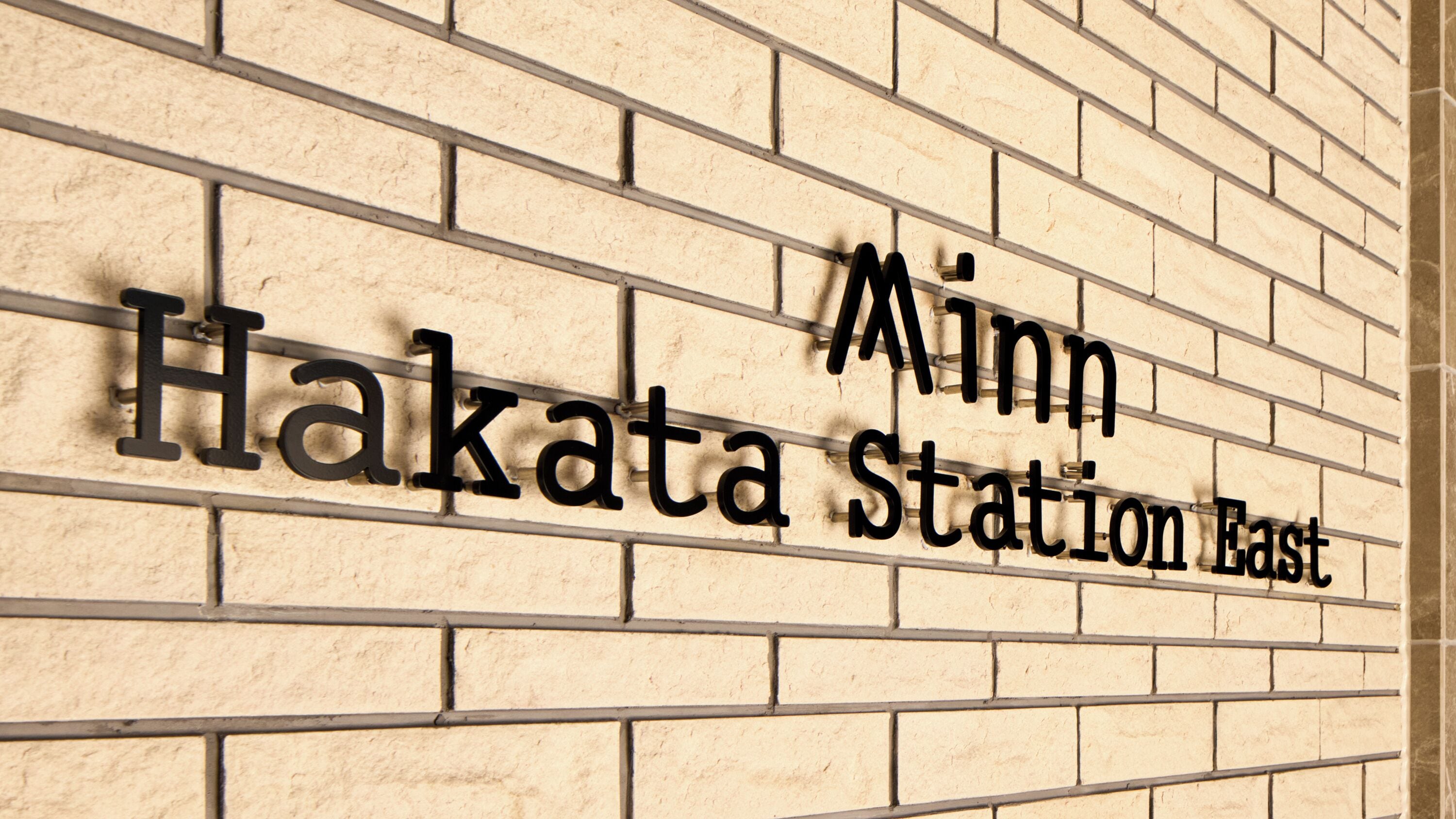 En murstensvæg med teksten 'Minn Hakata Station East', der angiver placeringen.