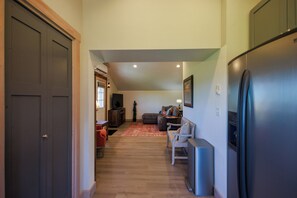 Ein Flur mit einer dunklen Tür, ein Wohnbereich mit einer Couch und einem Couchtisch, einem Kühlschrank und einem Holzboden.