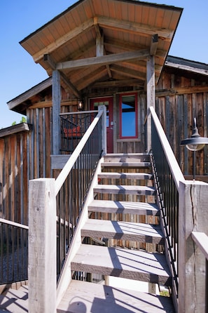 A wooden staircase leading to a building with a red door and a balcony.
