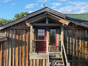 Eine Holzdiele mit roter Tür, einem kleinen Balkon und einer Treppe zum Eingang.