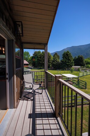 A wooden deck with a chair and table, a view of a fenced pasture, and distant mountains.