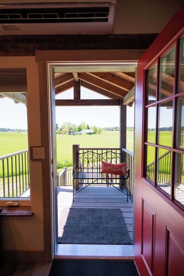 A wooden deck with a bench and a red door leading to a view of a green field.