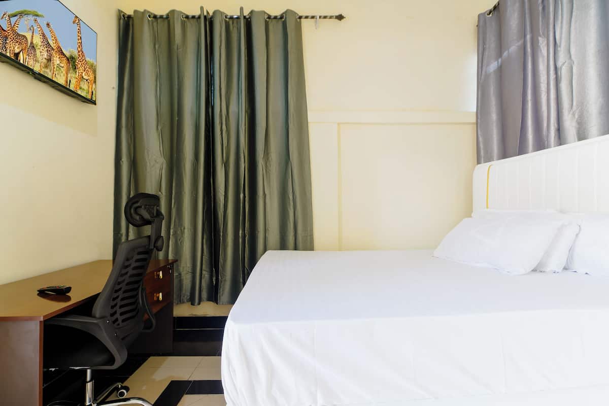 A hotel room with a bed, a desk with a chair, a television mounted on the wall, and curtains.