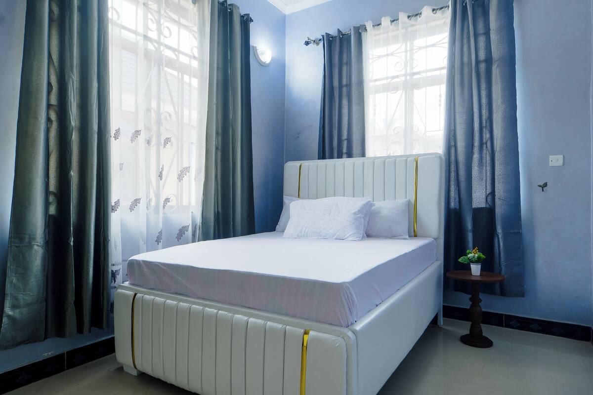 A bedroom with a bed, curtains, a small table with a plant, and a radiator.