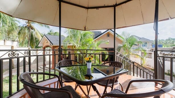 A covered outdoor seating area with a glass table, wicker chairs, and a vase with flowers.
