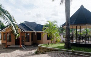 A building with a curved roof, a covered outdoor seating area, and a stone pathway. - Cozy Tanzania  (Dar es Salaam)