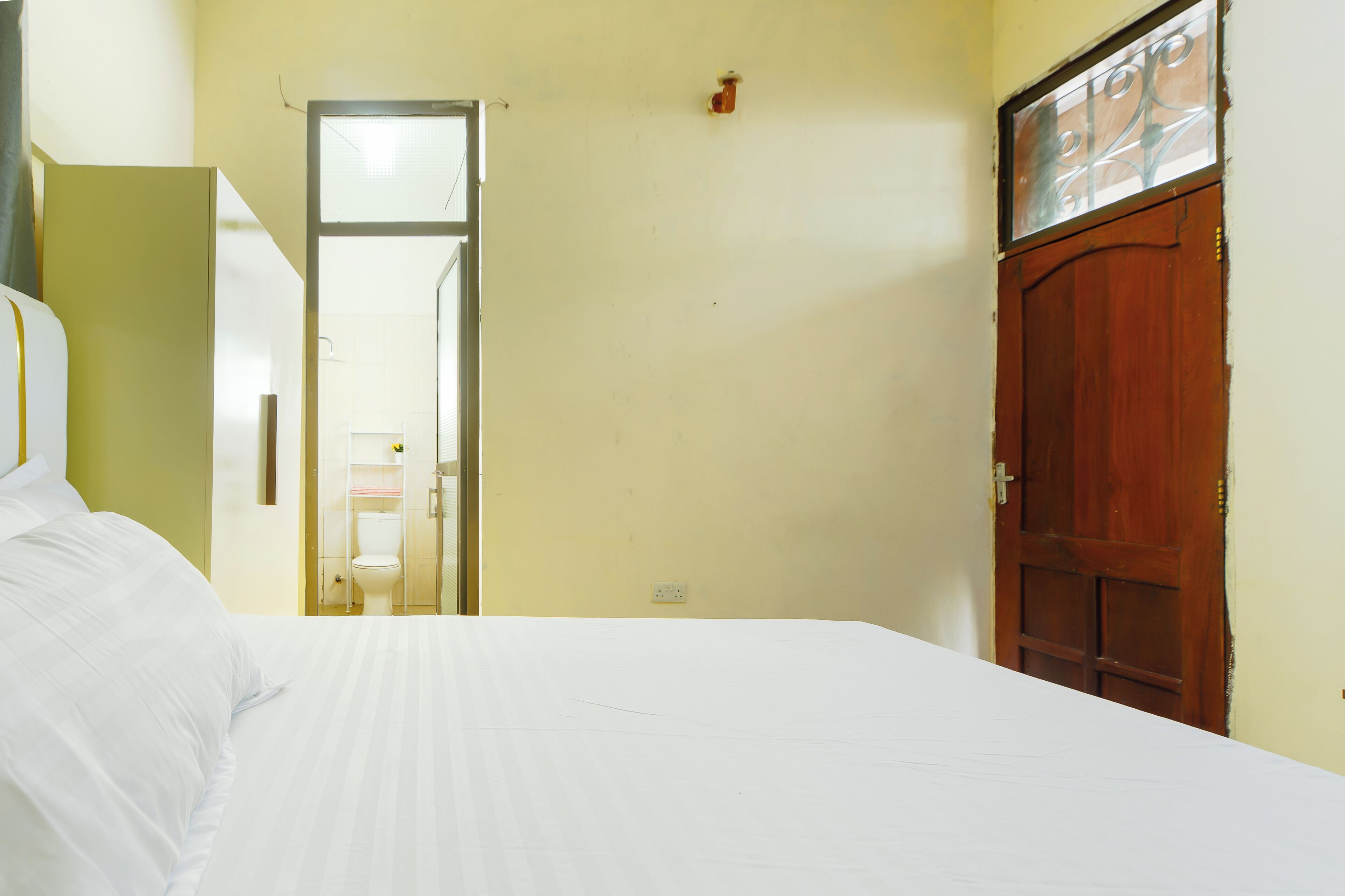 Une chambre à coucher avec un lit, une porte en bois et une salle de bain visible à travers une porte ouverte.