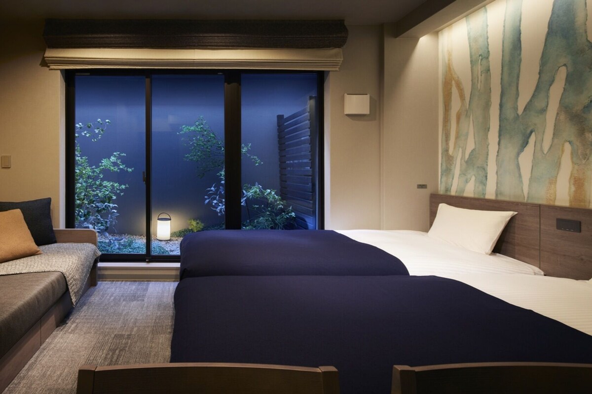 Ein Hotelzimmer mit einem Bett, einer Couch und Blick auf Grün durch ein Fenster.
