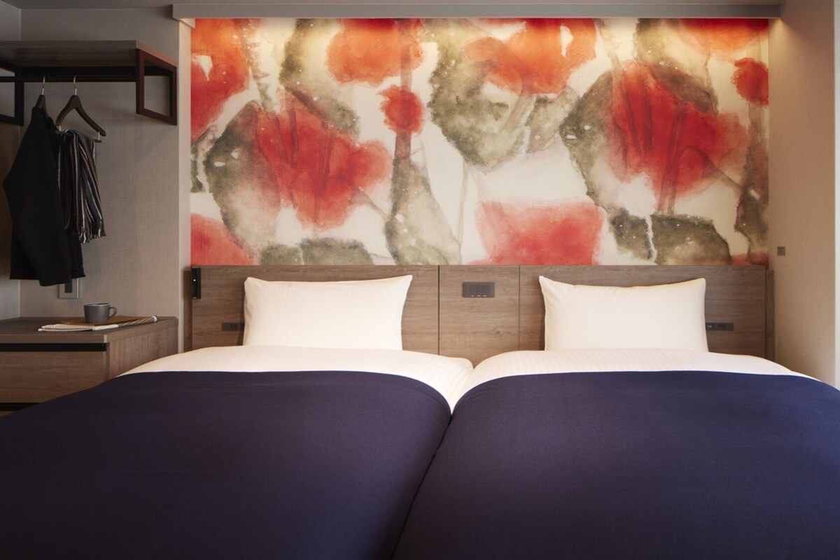 Ein Hotelzimmer mit einem Bett, einem Nachttisch, einem Wandbild und einem Kleiderständer.