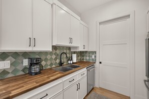 A kitchen with white cabinets, a wooden countertop, a coffee maker, a sink, and a dishwasher. - Getaway on the Henry's Fork (Saint Anthony)