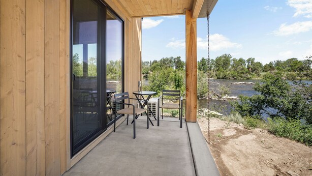 Esterno in legno con una porta in vetro, patio in cemento e vista su un fiume e alberi.