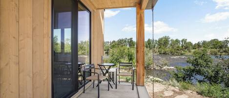 A wooden exterior with a glass door, a concrete patio, and a view of a river and trees.