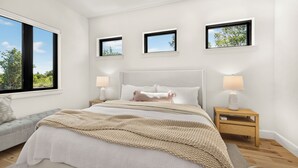 Una camera da letto con un'ampia finestra, un letto con testiera, comodini con lampade e tre quadri appesi al muro.