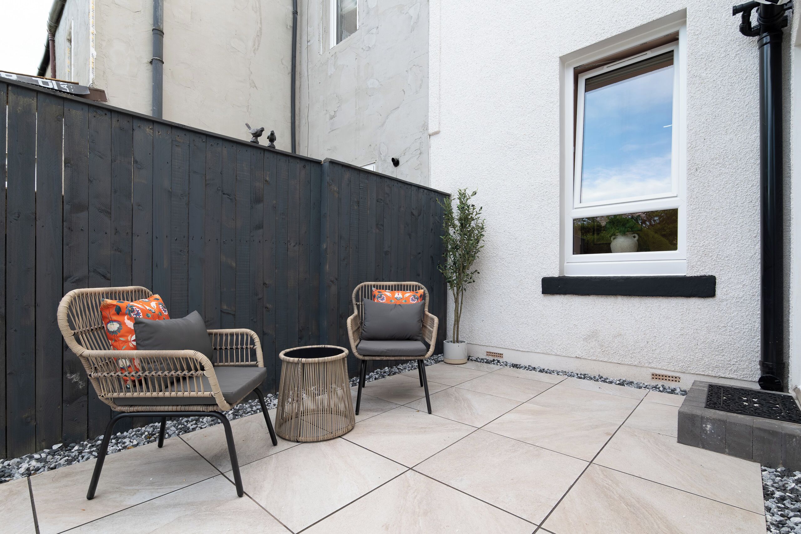 An outdoor patio area with two wicker chairs, a small round table, and a potted plant.