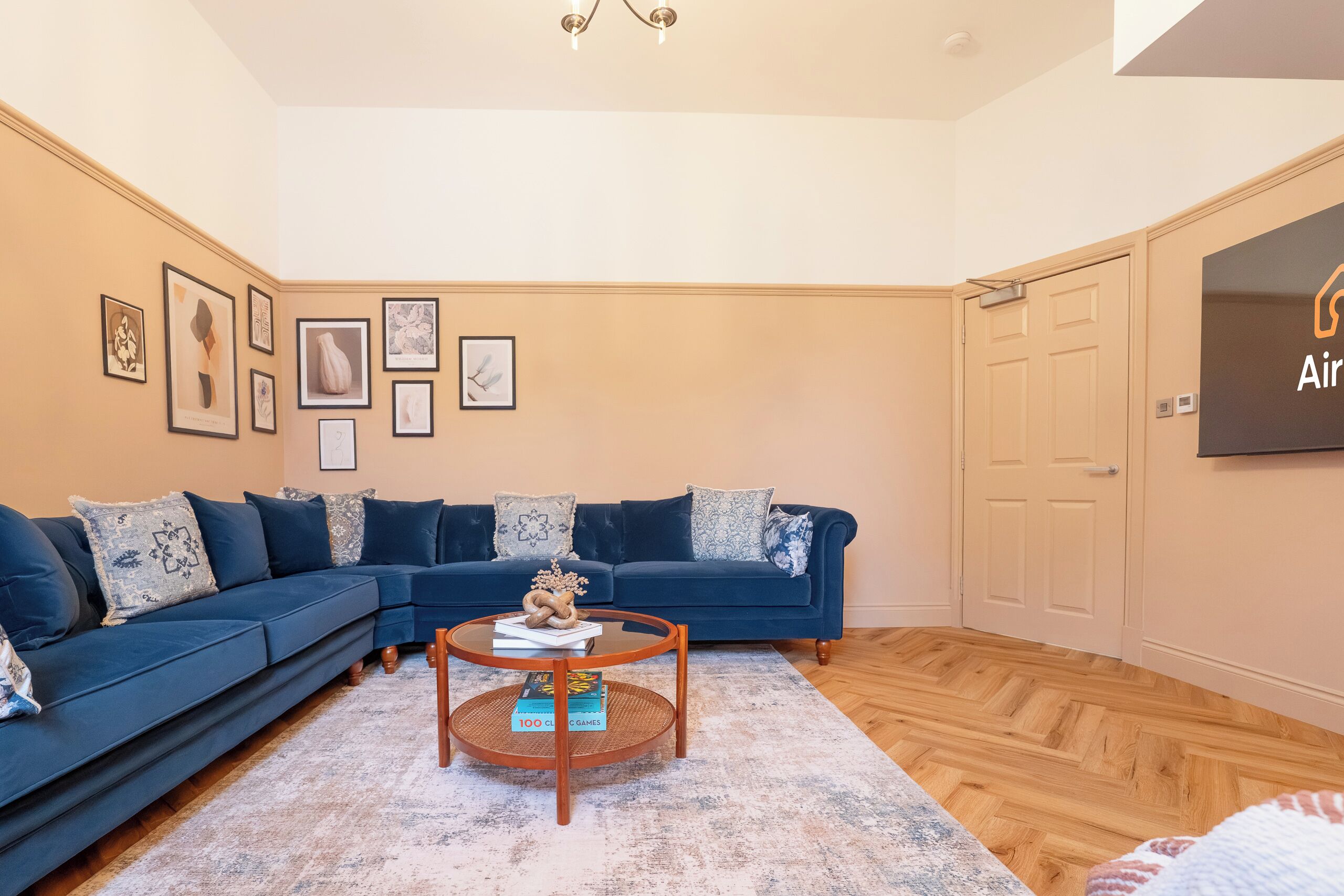 Een woonkamer met een donkerblauwe bank, een ronde houten salontafel en een vloerkleed met een patroon.