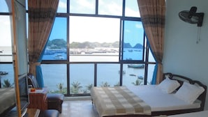 Een kamer met een bed, een bureau, een stoel en een televisie. Er is een groot raam met uitzicht op de zee en boten.
