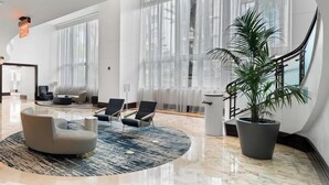 Un amplio vestíbulo con piso de mármol, ventanas grandes y asientos modernos.