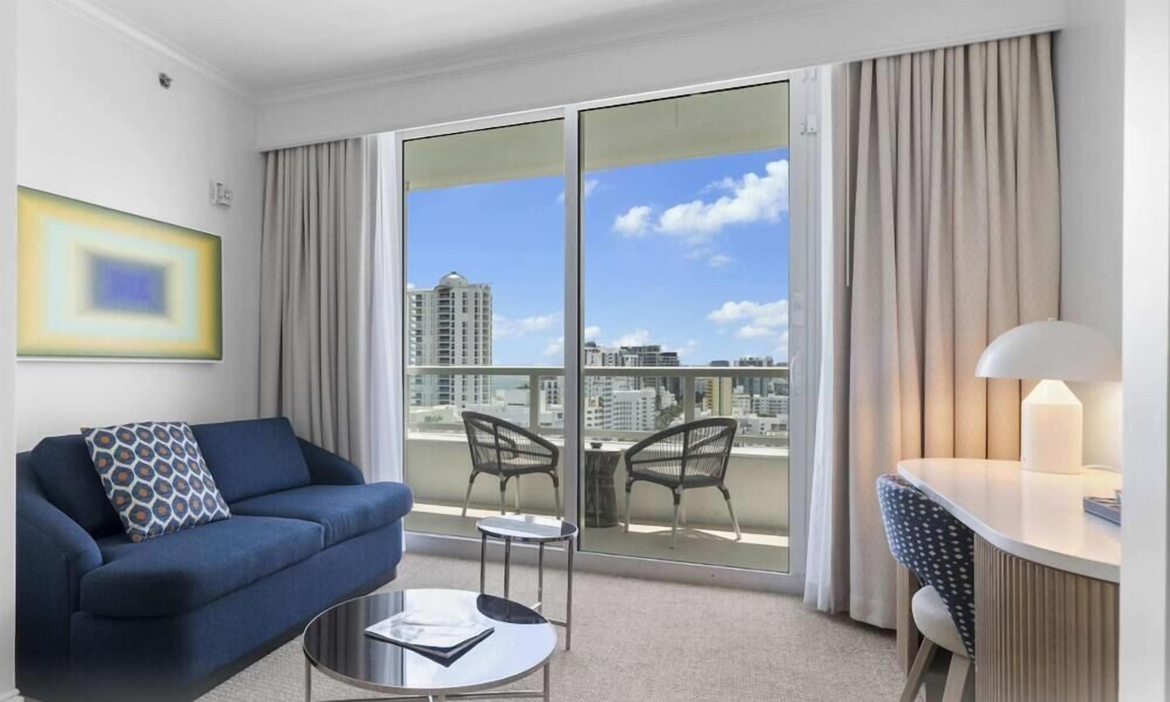 A hotel room with a balcony, a sofa, a small table, and a chair.