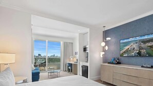 Una habitación de hotel moderna con una cama grande, un escritorio, un balcón con vistas a la ciudad y un televisor de pantalla plana montado en la pared.