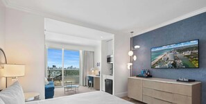 Ein modernes Hotelzimmer mit einem großen Bett, einem Schreibtisch, einem Balkon mit Stadtblick und einem an der Wand befestigten Flachbildfernseher.