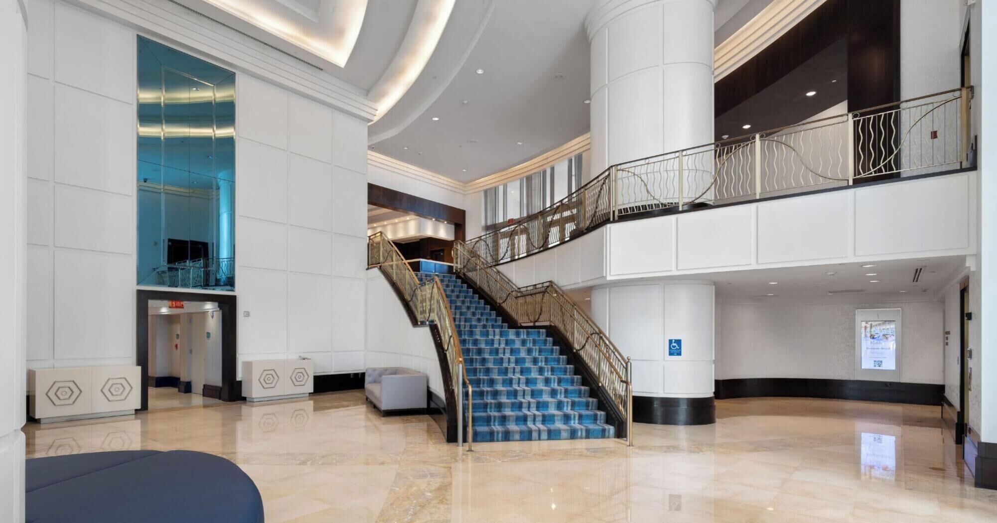 Un hall d’entrée spacieux avec un escalier central, un balcon au deuxième étage et un design moderne.