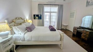 A bedroom with a bed, bedside tables, a TV, a window with curtains, and a desk with a chair.