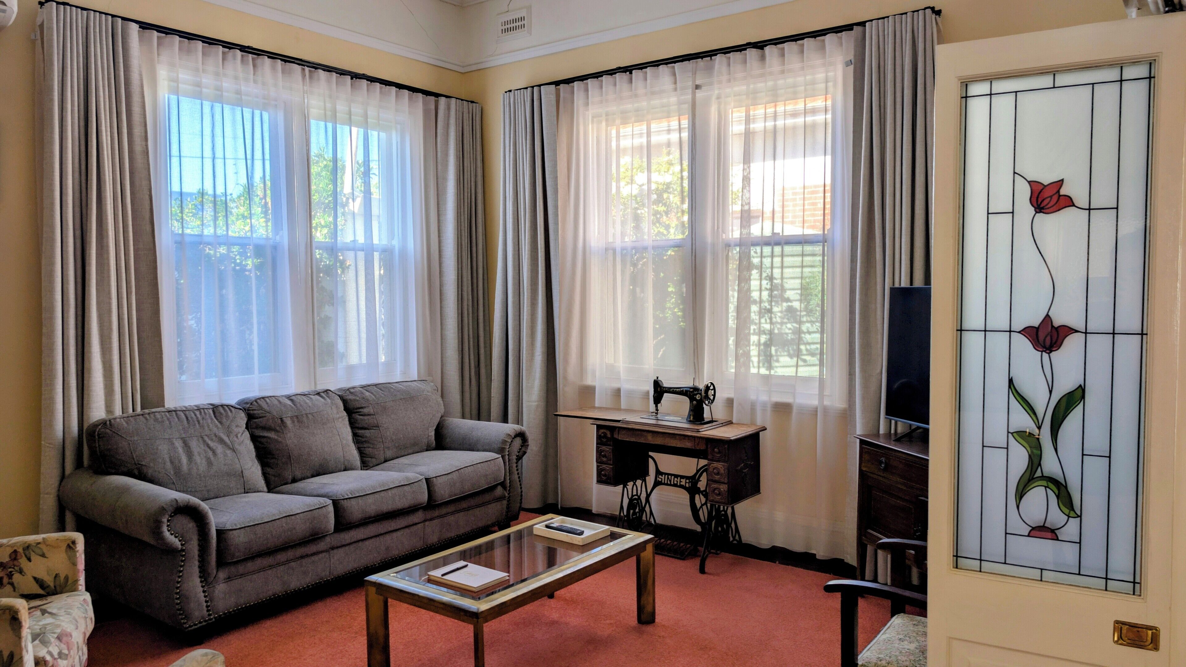 A living room with a sofa, a sewing machine, a television, and a stained glass window.