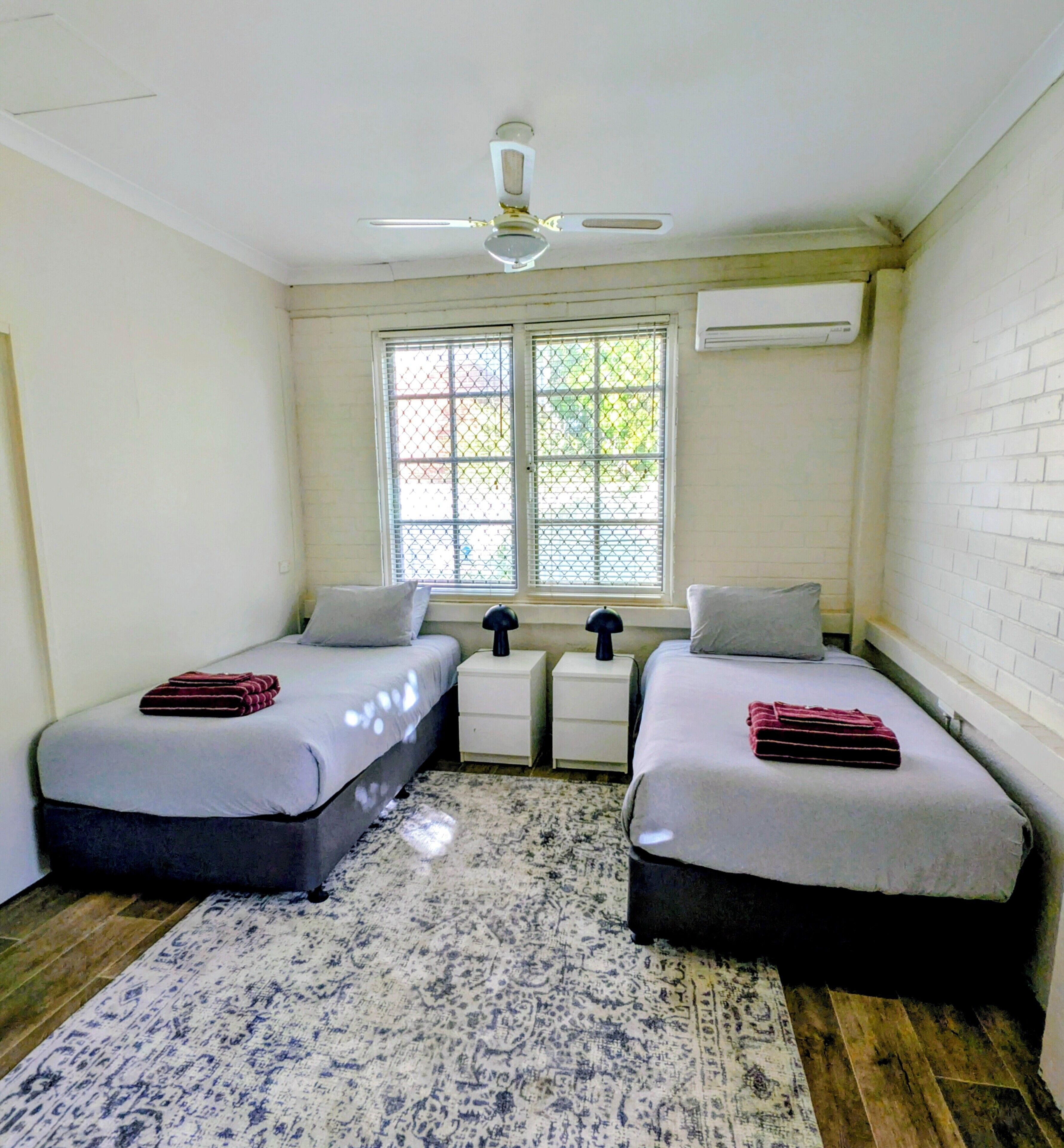 A bedroom with two beds, a ceiling fan, an air conditioning unit, and a window with a view.