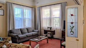 Un salon comprenant un canapĂ©, une table basse, une machine Ă coudre et une porte ornĂ©e dâun vitrail.