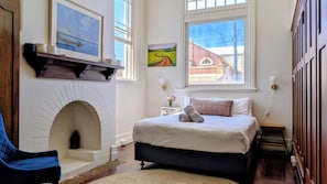 Un dormitorio con chimenea, una cama, una silla y dos ventanas.