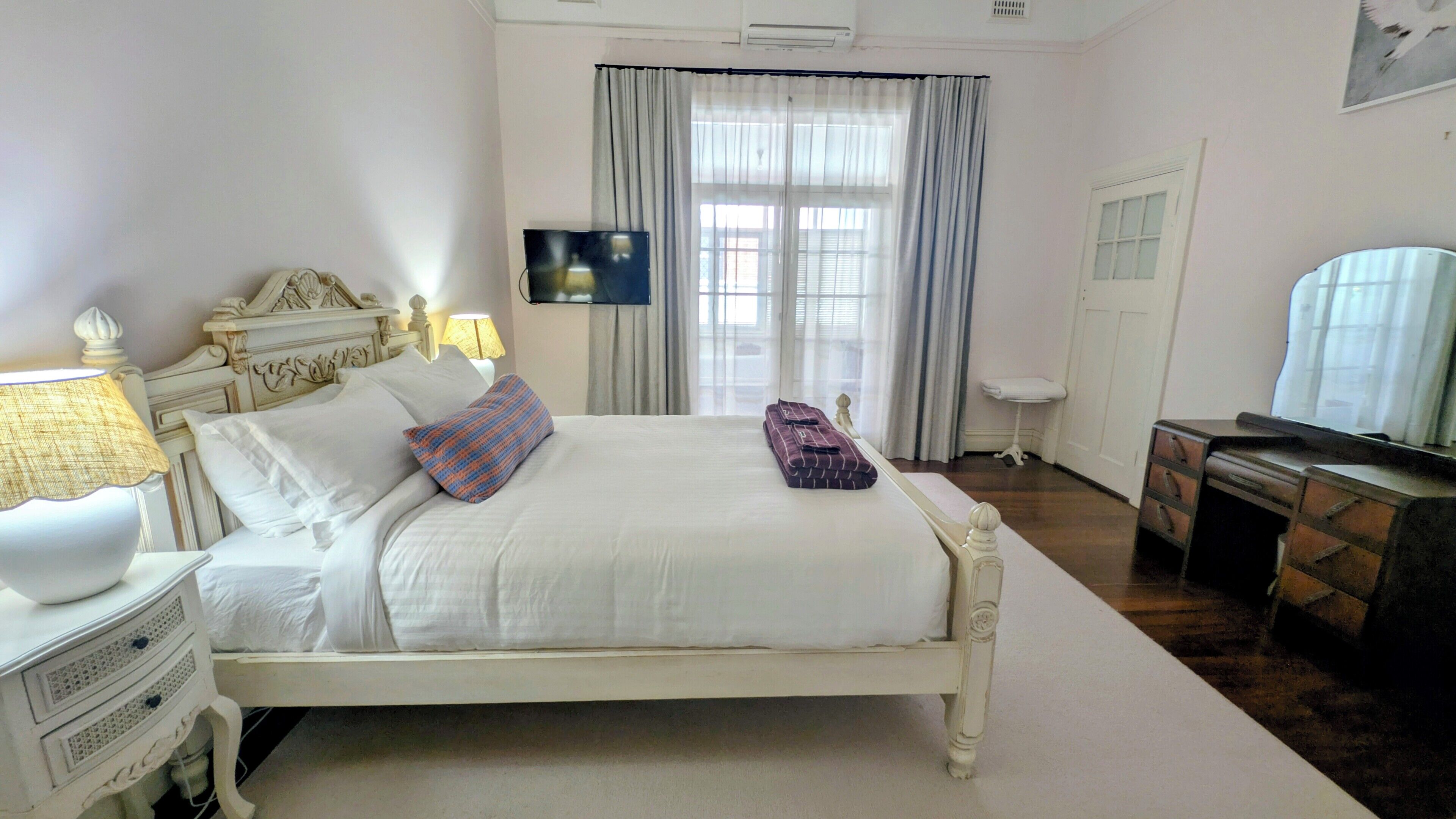A neatly made bed with pillows, a bedside lamp, a flat-screen TV, and a desk with a chair.